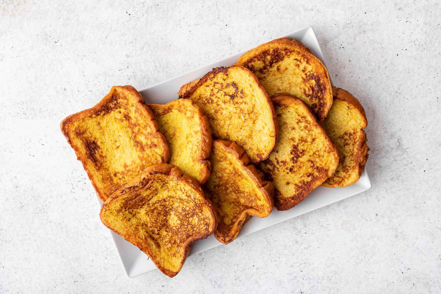 Ricetta del Pain Doré alla Brioche Fatto in Casa (Facile!) 6 Fette di French toast di brioche impilate su un piatto rettangolare bianco.