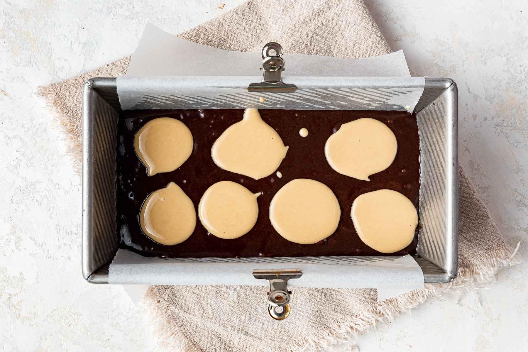 Cucchiai di tahini crudo sopra l'impasto dei brownies in uno stampo da plumcake.