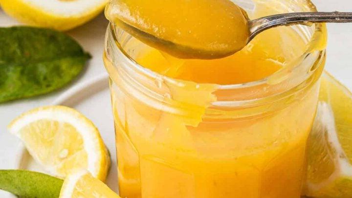 **Lemon Curd al Microonde in Piccola Quantità** 9 Barattolo di vetro di crema al limone al microonde con un cucchiaio che rimuove una porzione.
