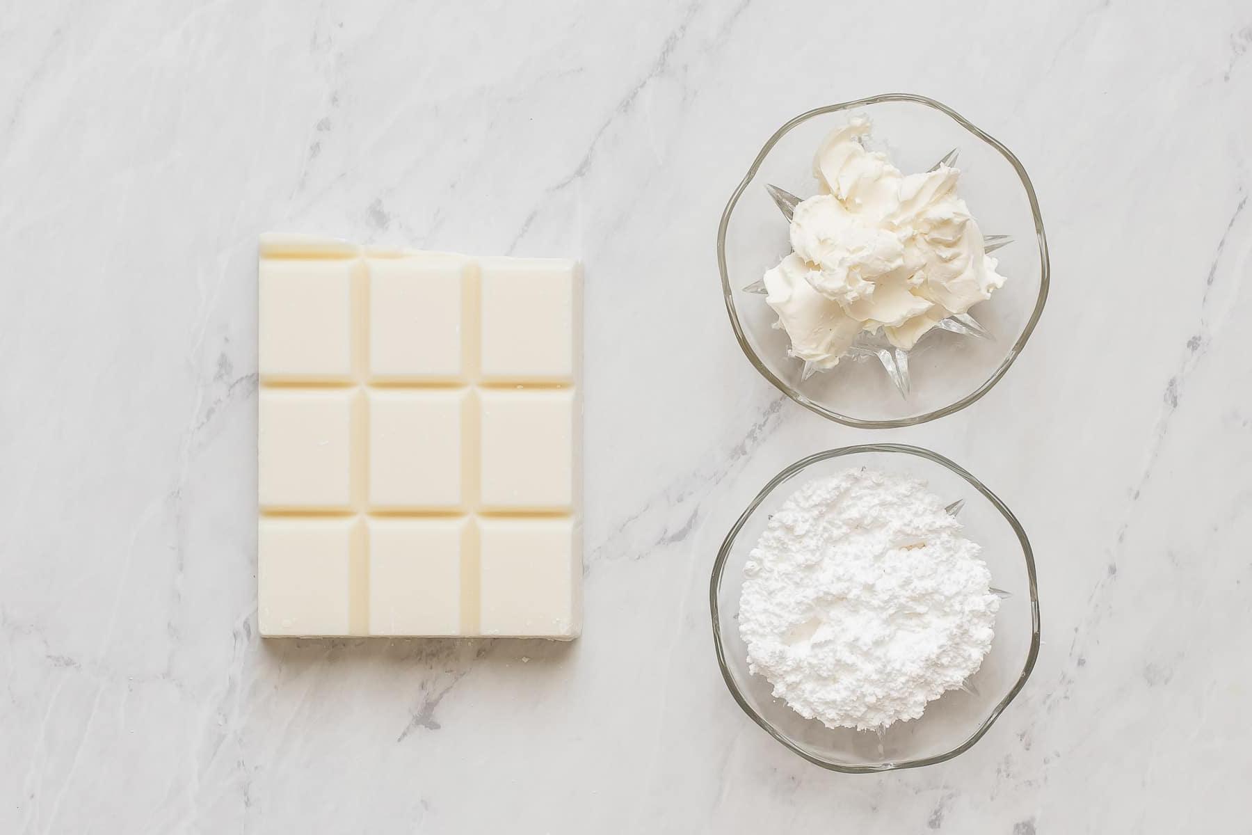 Cioccolato bianco, formaggio cremoso e zucchero a velo su tavolo bianco.