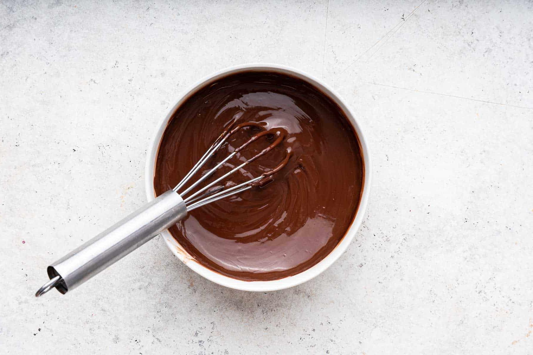 Cheesecake al caffè 9 Cioccolato fuso in una ciotola bianca con una frusta, pronto per la ganache.