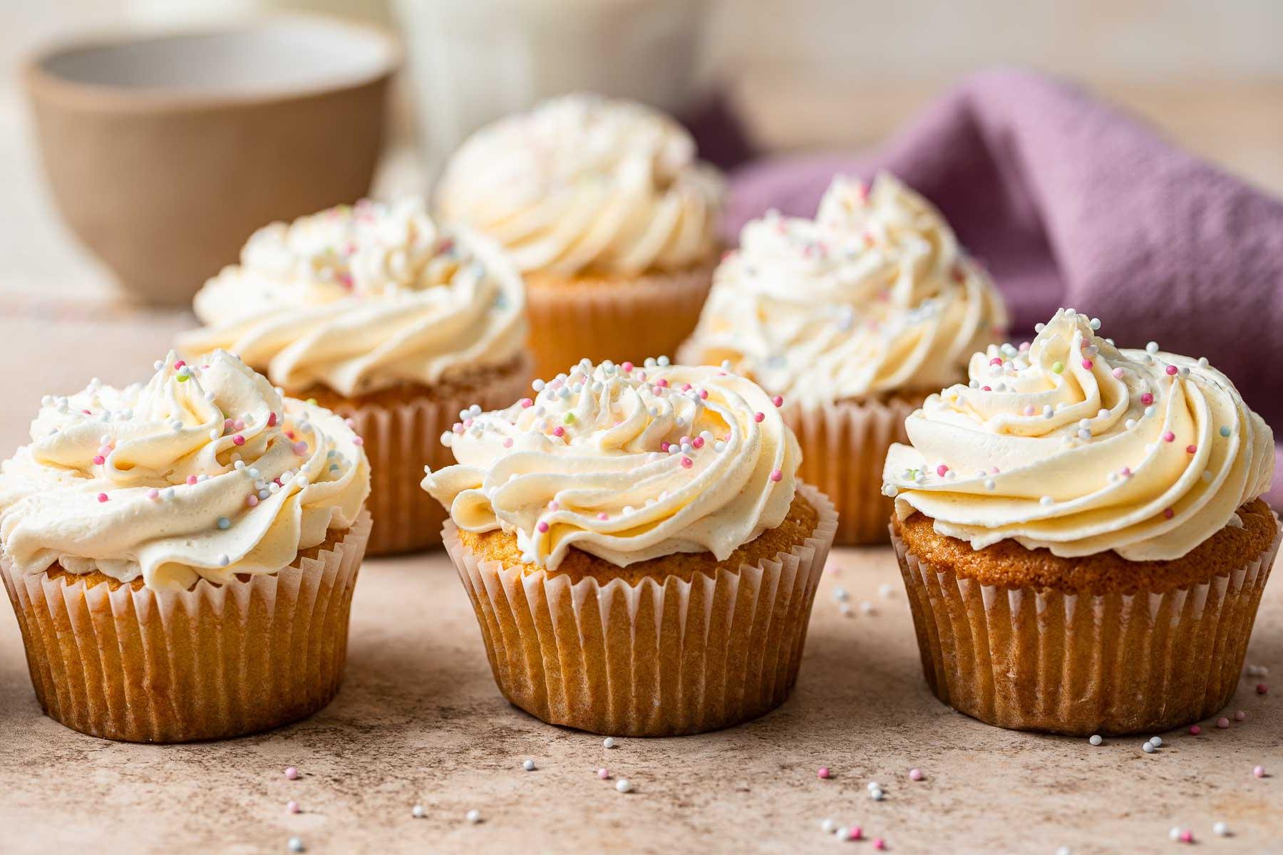 Cupcake alla vaniglia in piccola dose su un piano del tavolo, con glassa abbondante.