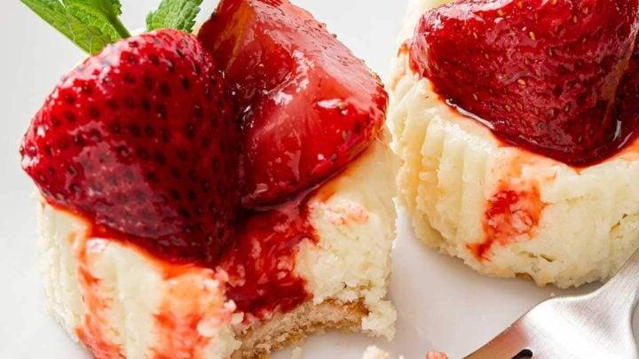 Mini Cheesecake alla Fragola 9 Due mini cheesecake alle fragole su un piatto con una forchetta.