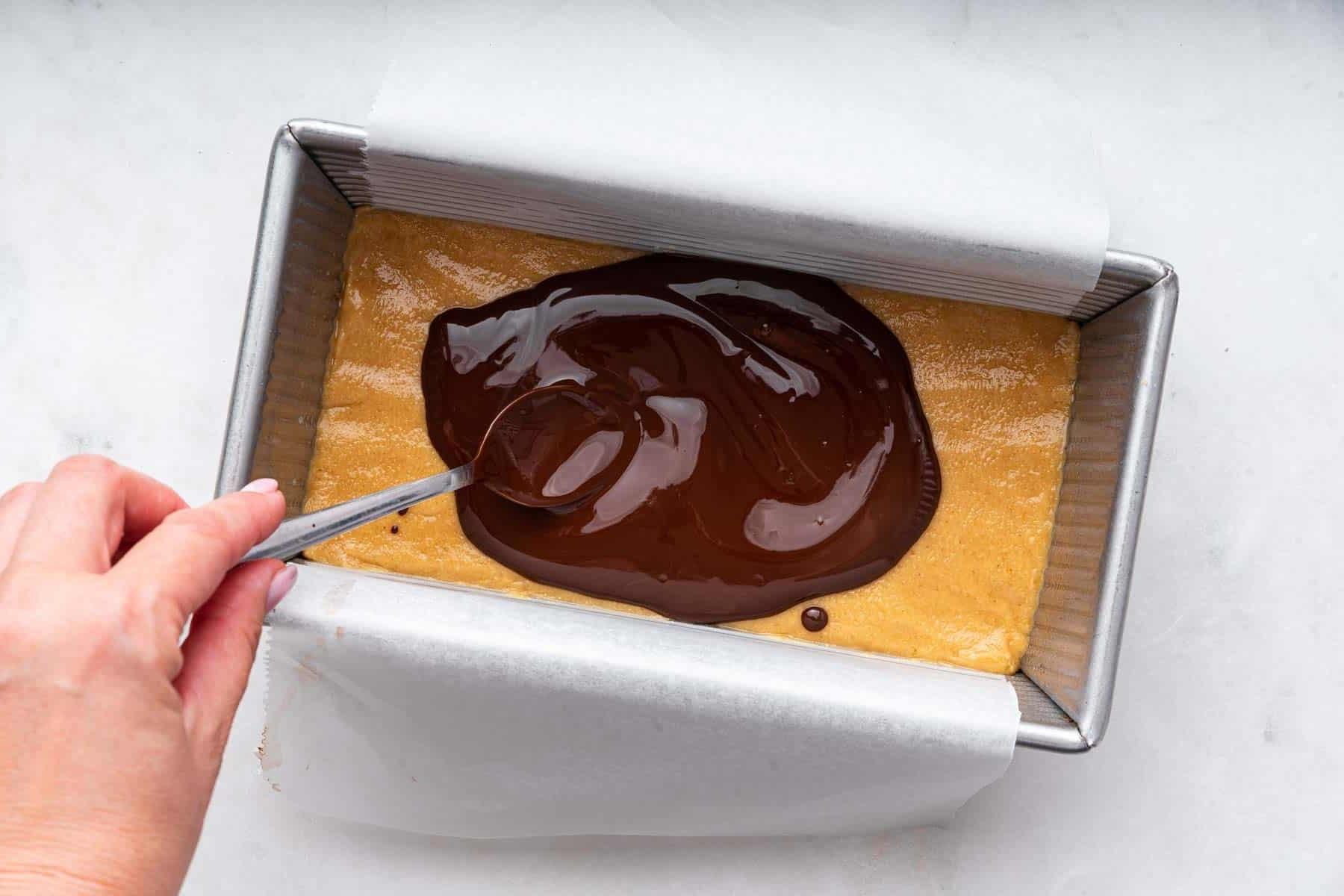 Barrette al Burro di Arachidi (Senza Cottura) 10 Mano che spalma cioccolato fuso su crosta dorata in teglia da pane.