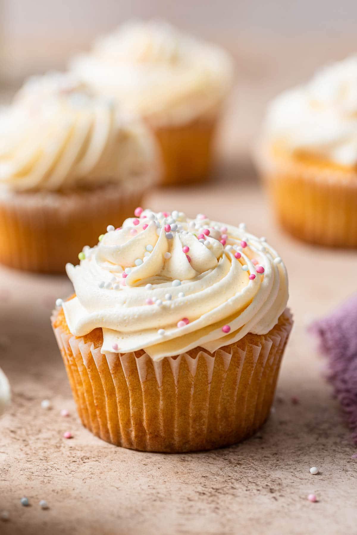 Piccolo Lotto di Cupcakes alla Vaniglia 10 Quattro cupcake alla vaniglia in piccola dose con glassa bianca e zuccherini su una superficie di marmo.