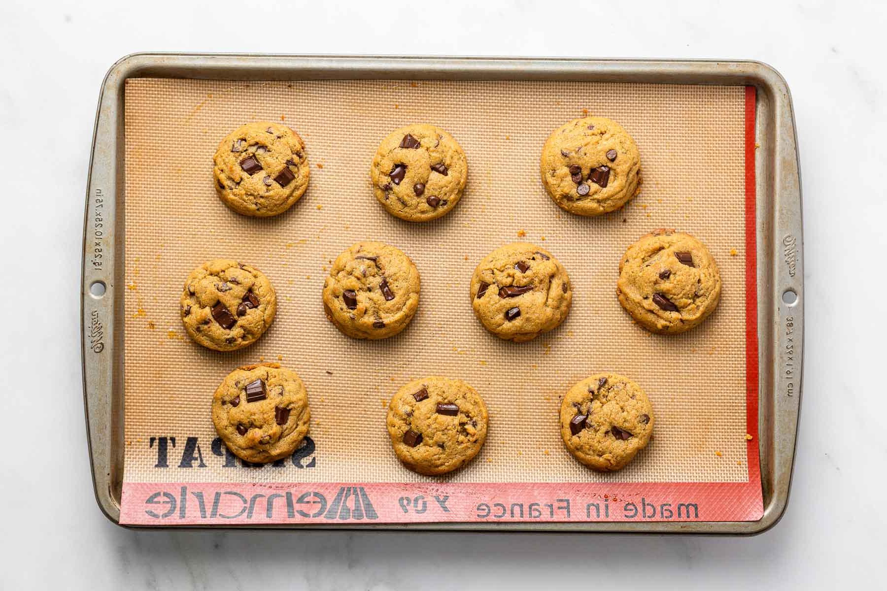 Dieci biscotti al cioccolato con zucchero di canna cotti su una teglia con tappetino in silicone.