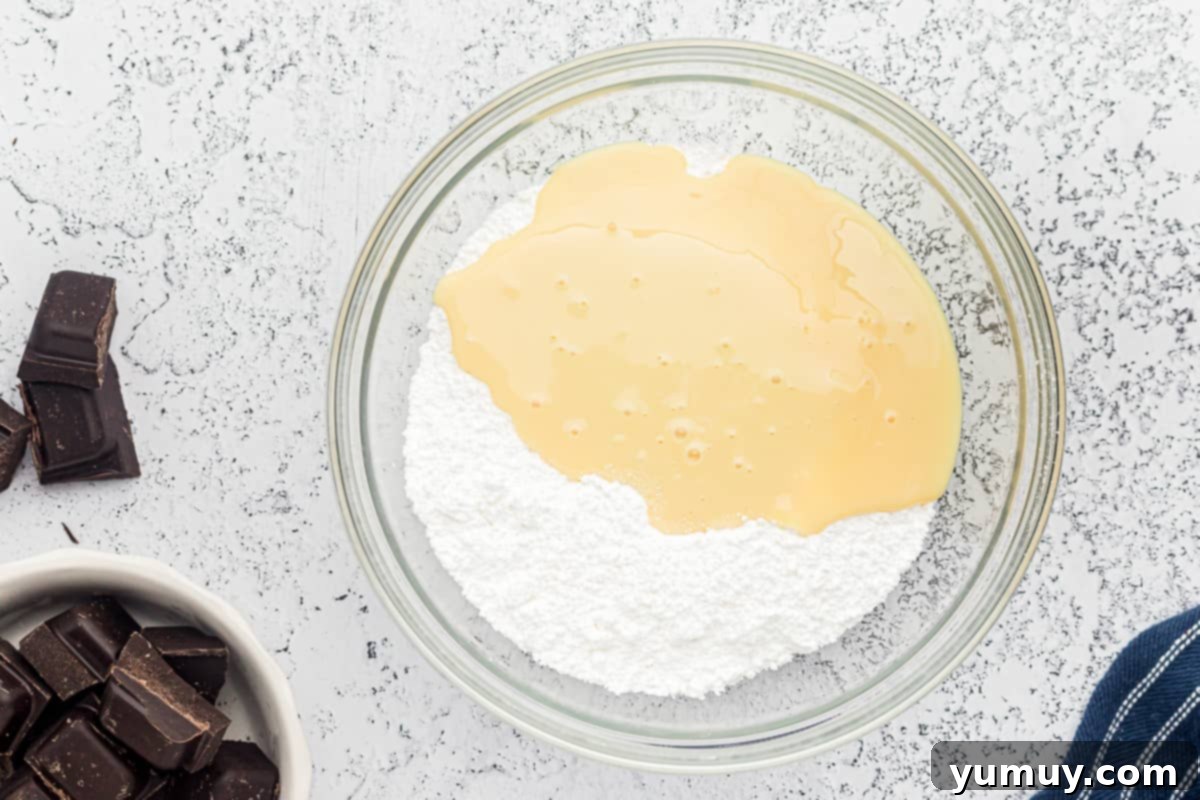The initial mixing stage of sweetened condensed milk and powdered sugar for the peppermint filling in a glass bowl.