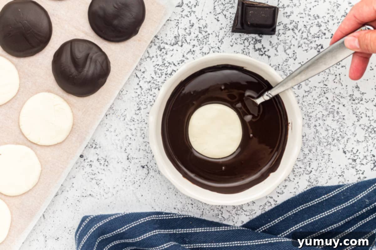 A peppermint patty being carefully dipped into a bowl of perfectly melted dark chocolate.