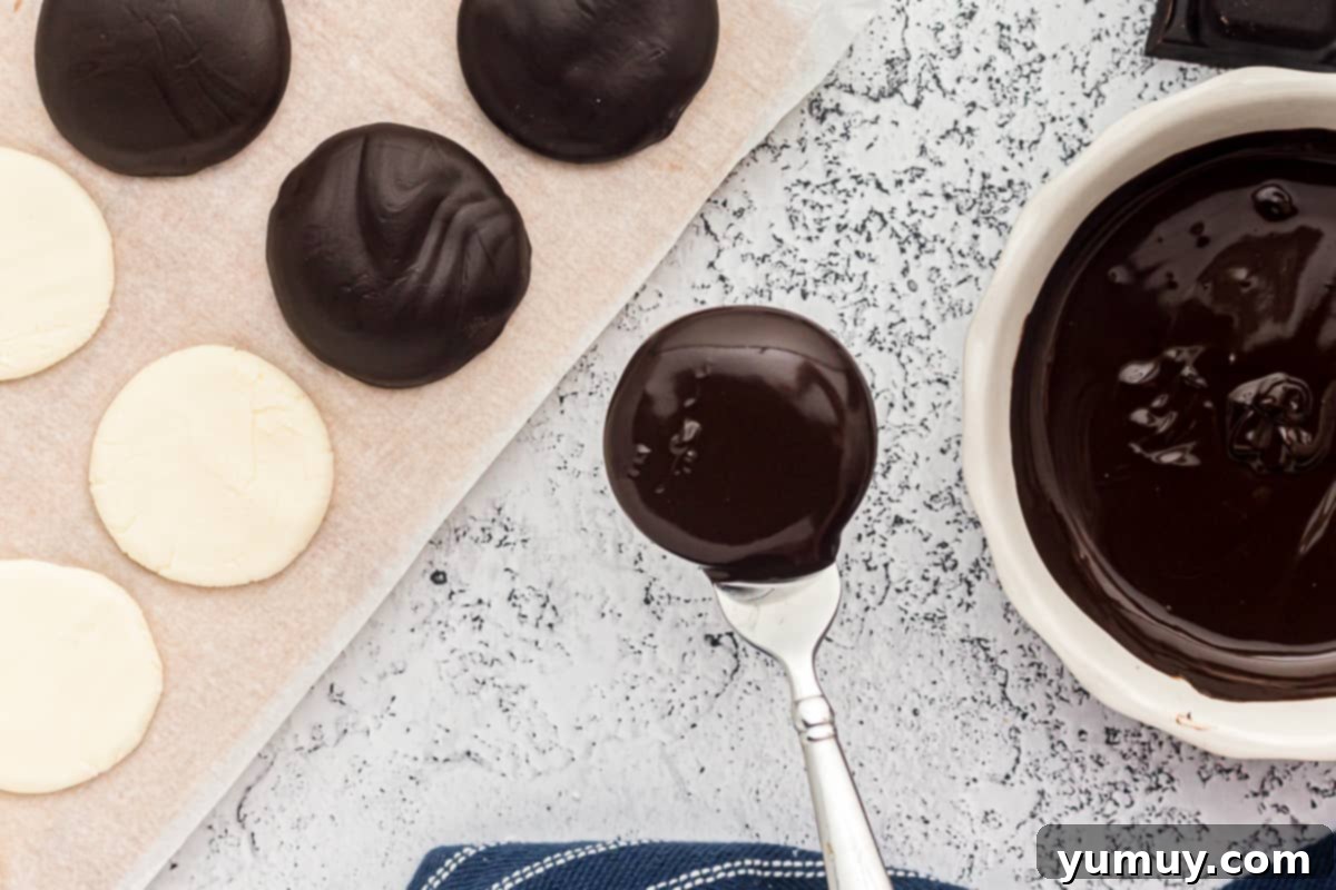 A freshly chocolate-coated peppermint patty being lifted from the melted chocolate, ready to be placed on parchment paper to set.