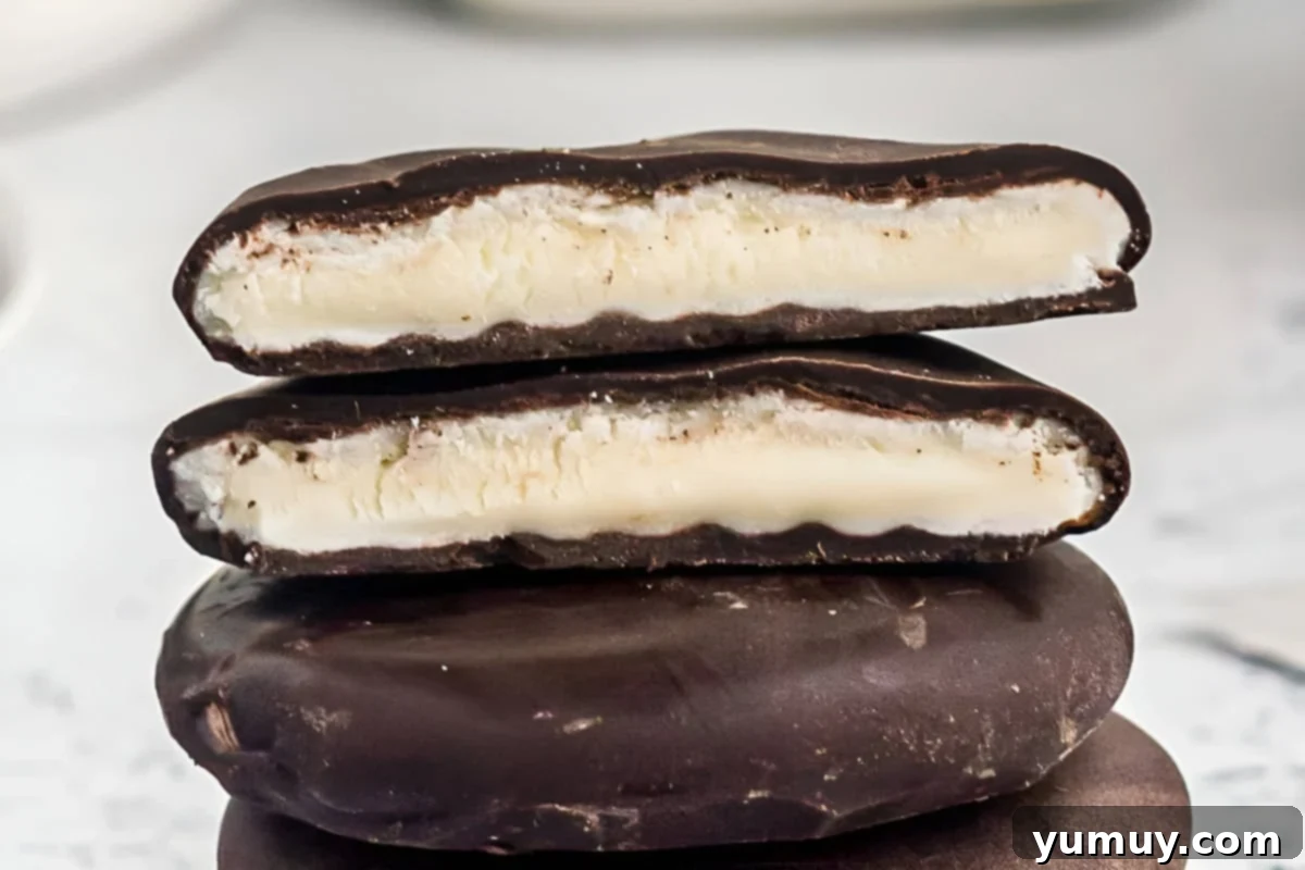 A perfectly halved peppermint patty stacked on top of whole patties, revealing the smooth white peppermint filling inside a dark chocolate shell.