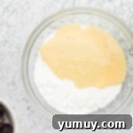 Sweetened condensed milk and half of the powdered sugar being mixed in a glass bowl.