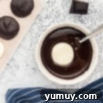 A peppermint patty being dipped into a bowl of smooth, melted dark chocolate using a fork.