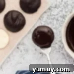 A freshly chocolate-coated peppermint patty being lifted from melted chocolate with a fork, ready to set.