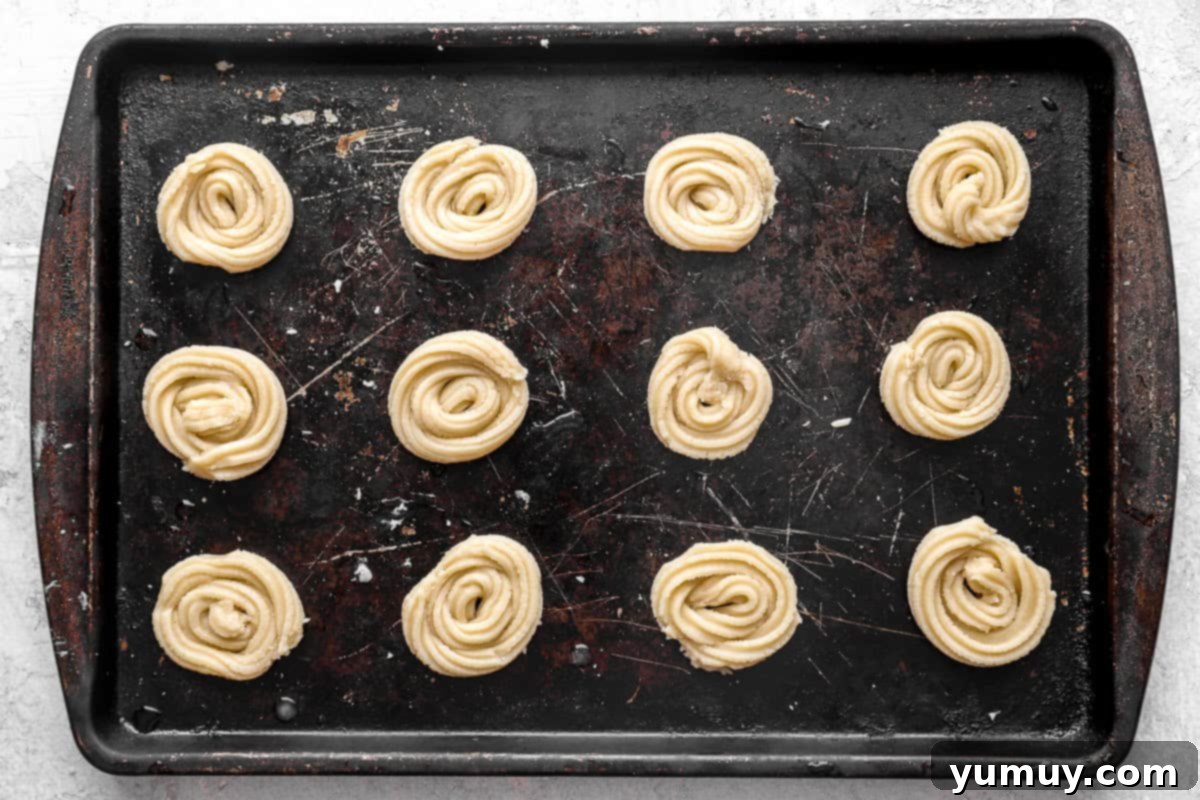 Pure Butter Delights 13 Unbaked butter cookie dough, some scooped, some piped into swirls, neatly arranged on a parchment-lined baking sheet.