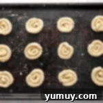 Pure Butter Delights 8 Unbaked butter cookie dough portions lined up on a parchment-lined baking sheet.