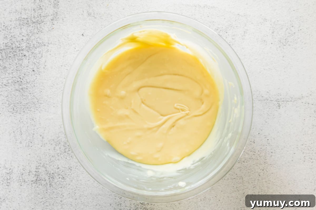 Haunted Fudge Delights 10 Smoothly melted white chocolate and condensed milk mixture in a clear glass bowl, ready for the next step.