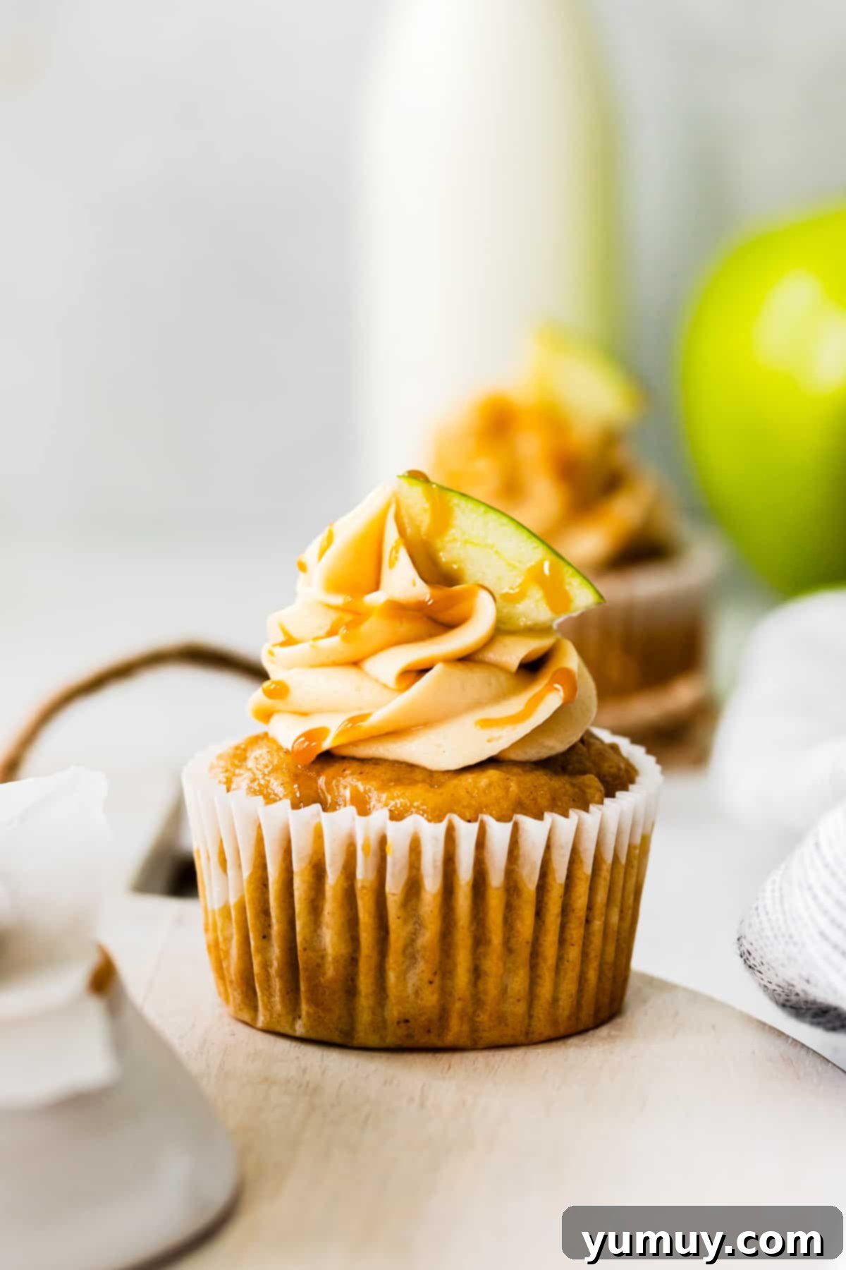 apple cupcakes topped with caramel frosting, a drizzle of salted caramel, and an apple slice
