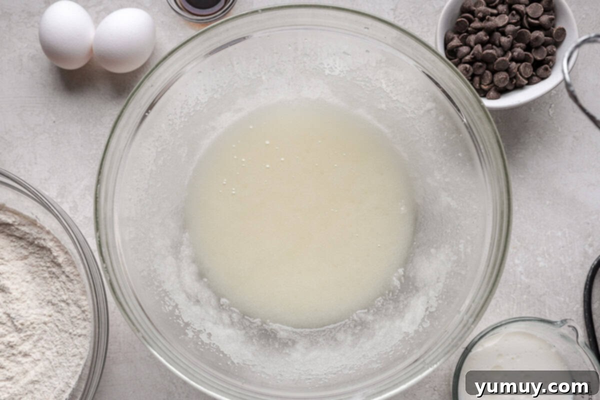Ultimate Chocolate Chip Cupcakes 7 A creamy mixture of vegetable oil and granulated sugar being blended in a large mixing bowl, showcasing its light and frothy consistency.