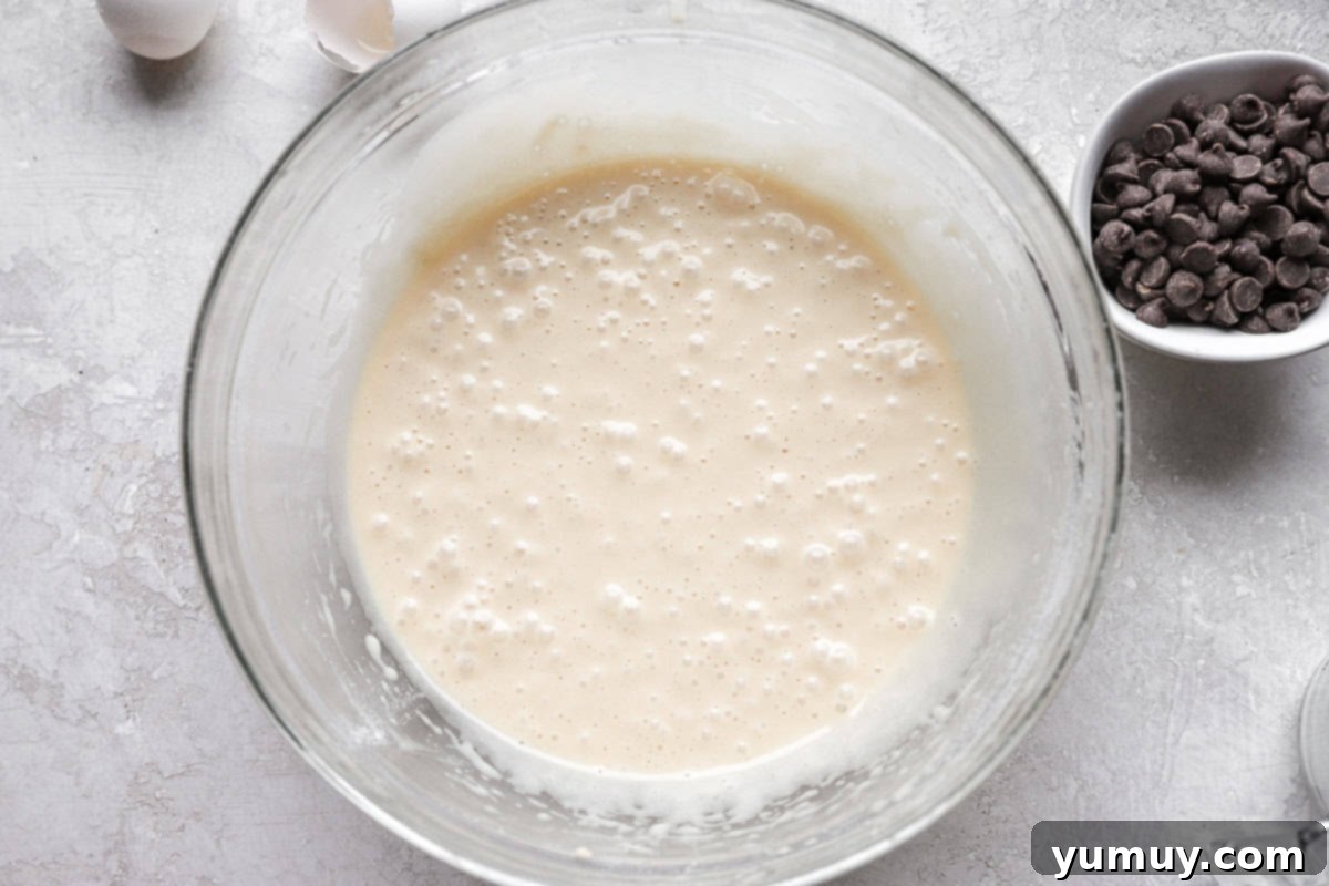 Ultimate Chocolate Chip Cupcakes 9 Rich chocolate chip cupcake batter, shimmering with melty chocolate chips, nestled in a pristine glass mixing bowl, ready for baking.