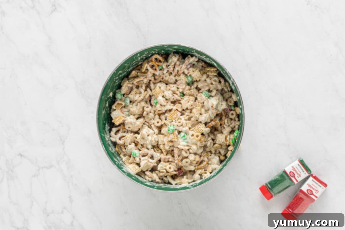 Chex Mix being coated evenly with melted white chocolate in a large mixing bowl.