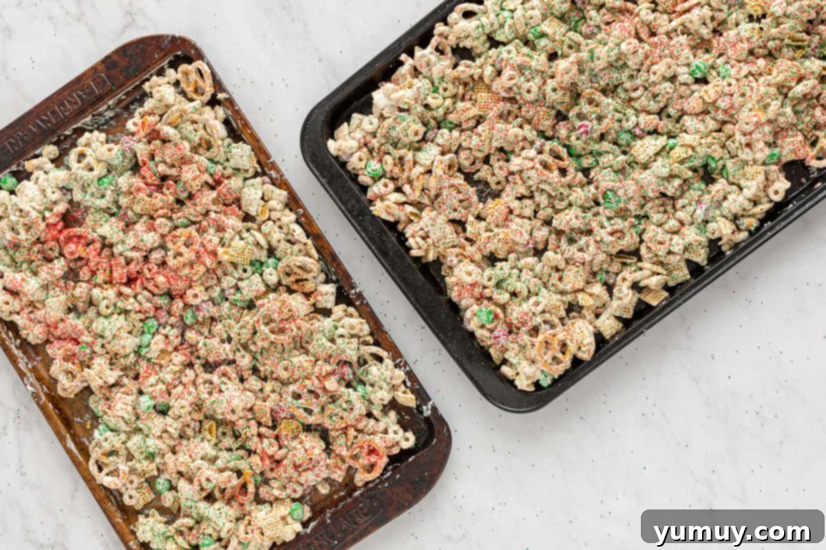 Finished Christmas Crack Chex Mix spread on parchment-lined baking sheets, adorned with red and green sprinkles, ready to set.