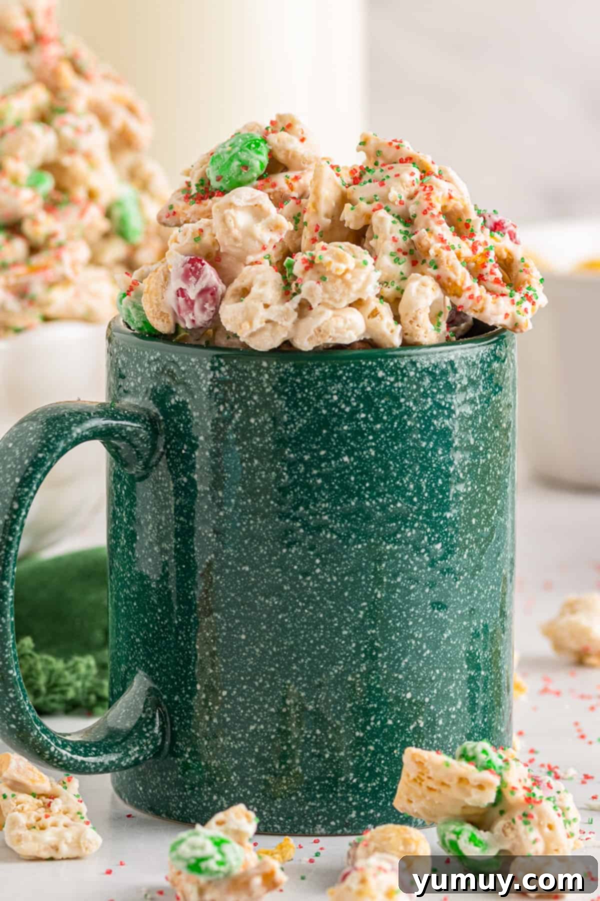 A green mug overflowing with vibrant Christmas Crack Chex Mix, ready to be enjoyed.