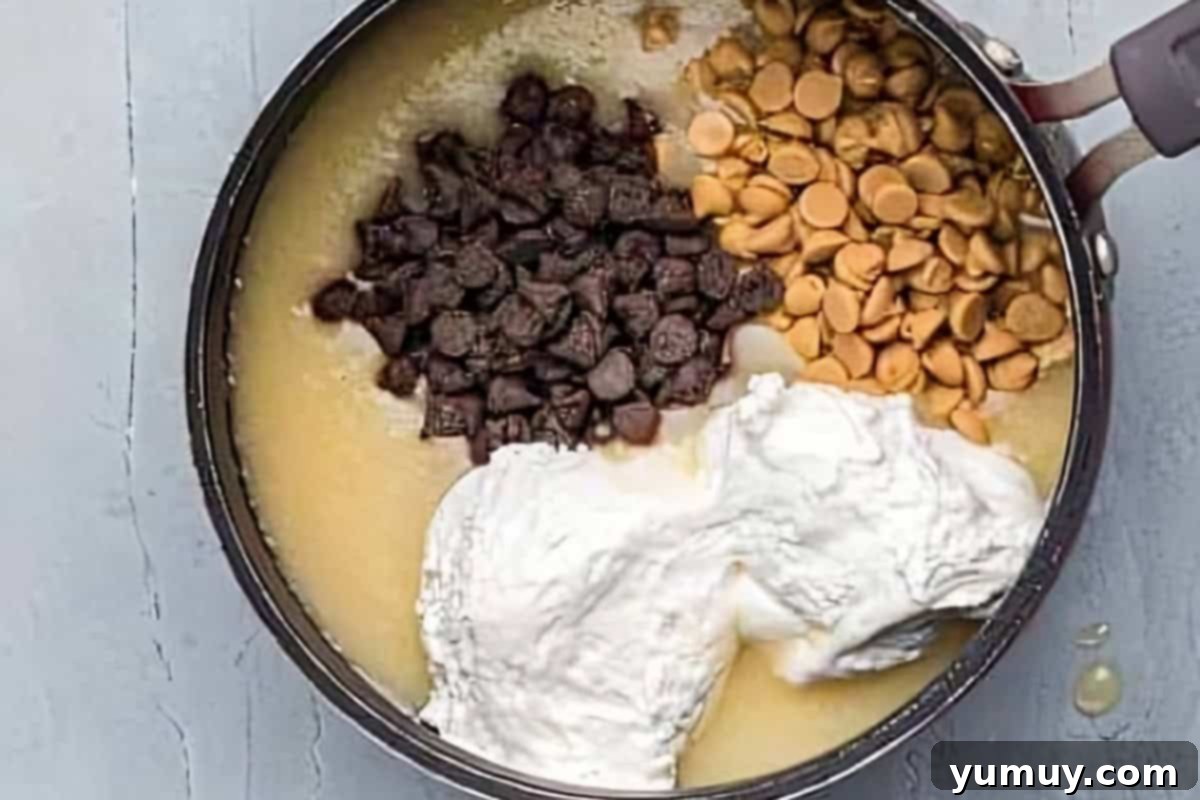 Butterfinger Bliss Fudge 12 Marshmallow fluff, chocolate chips, and peanut butter chips being stirred into hot fudge mixture in a saucepan