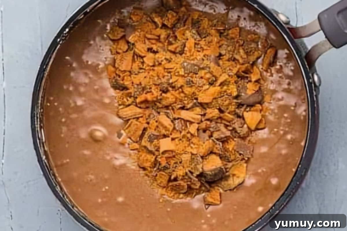 Butterfinger Bliss Fudge 13 Chopped Butterfinger candy pieces being stirred into the rich fudge mixture in a saucepan