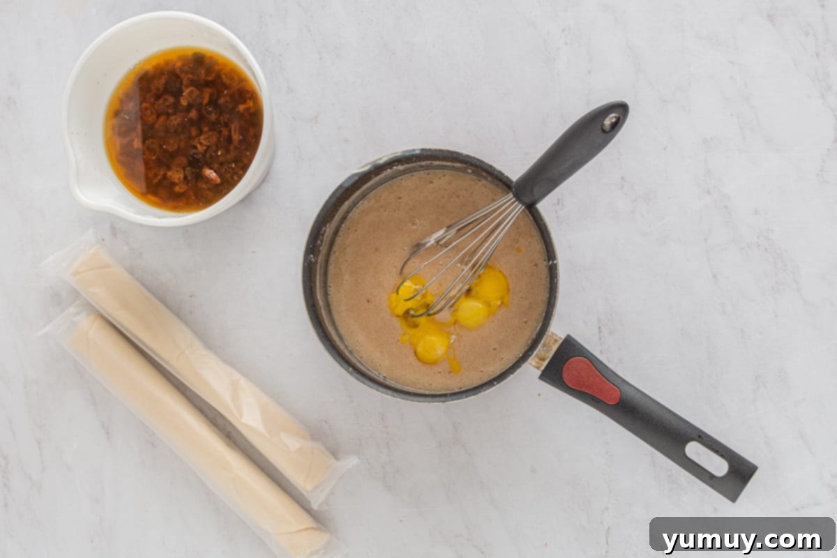 Velvet Raisin Bliss 20 A hand vigorously whisking egg yolks into a hot custard mixture in a saucepan, ensuring a smooth texture.
