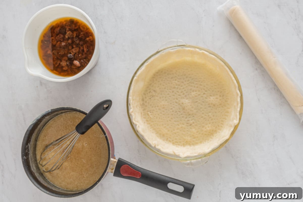 Velvet Raisin Bliss 21 A golden, par-baked pie crust in a fluted pan sits on a cooling rack, next to a saucepan holding the prepared pie filling.