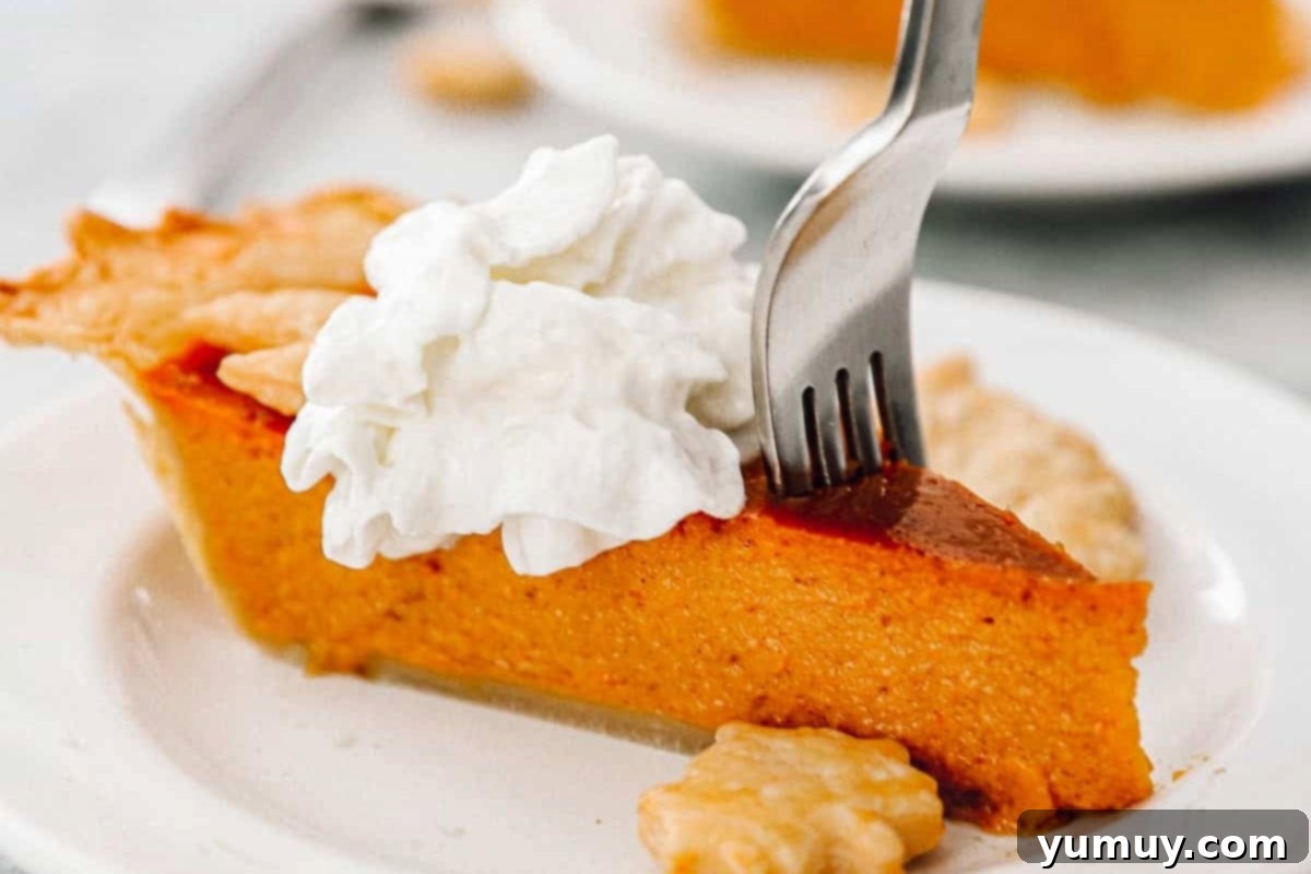 A fork poised to take a bite from a slice of pumpkin pie, generously topped with whipped cream and garnished with delicate pie crust leaves, all resting on a pristine white plate.