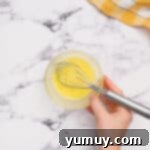 egg wash in a glass bowl with a whisk.