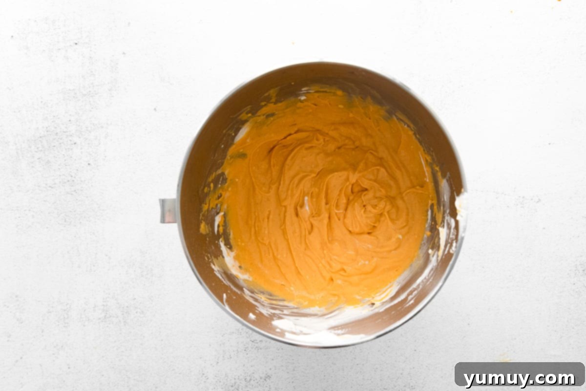 A rich mixture of pumpkin puree, softened cream cheese, and pumpkin pie spice blending smoothly in a metal stand mixer bowl, preparing the base for the mousse.
