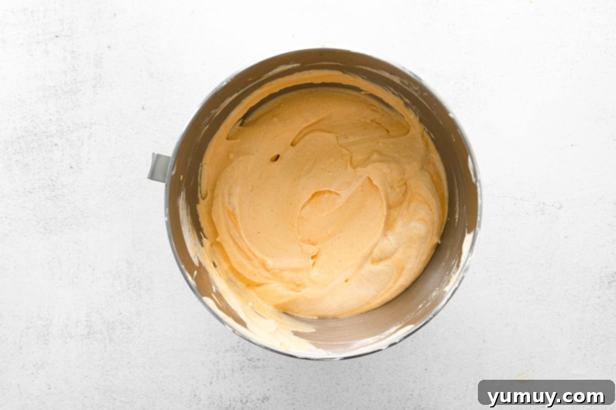 A large metal bowl holds a fluffy, creamy pumpkin mousse, illustrating the perfect texture after gently folding the whipped cream into the pumpkin base.