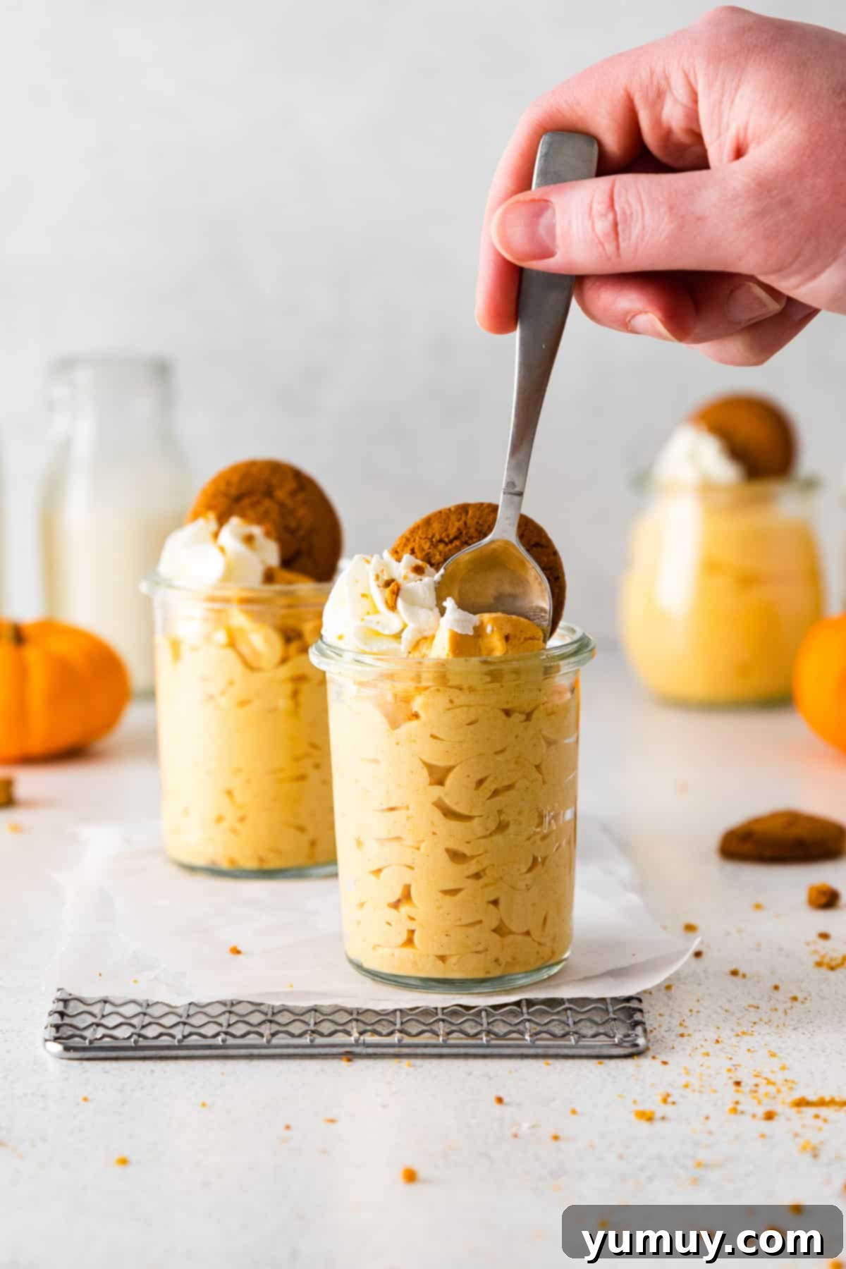 A hand gently holds a spoon, scooping a luscious bite of pumpkin mousse from a glass jar, showing its creamy texture and inviting appeal.