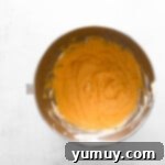 Creamy mixture of pumpkin puree, cream cheese, and pumpkin pie spice blending smoothly in a metal stand mixer bowl.