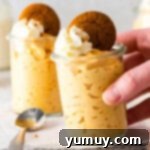 A hand reaching for a glass jar filled with perfectly chilled pumpkin mousse, garnished with whipped cream and crumbled cookies.