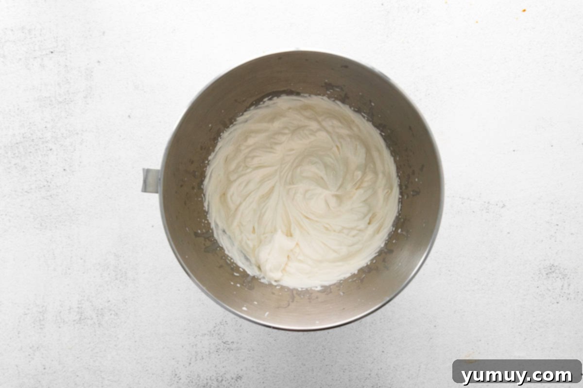 Freshly whipped cream with maple syrup and vanilla extract forms stiff peaks in a gleaming metal stand mixer bowl.