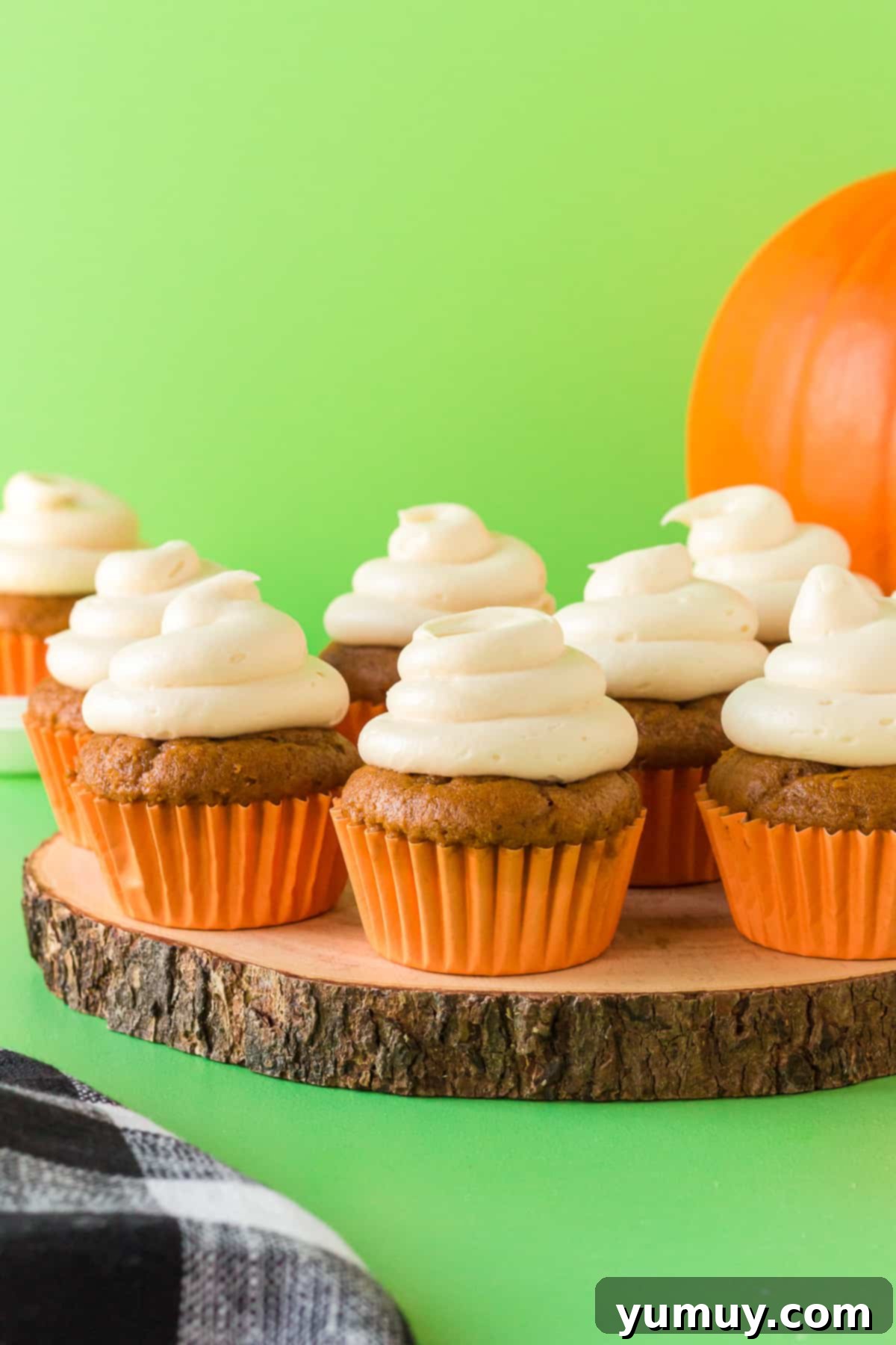 Delightful cake mix pumpkin cupcakes generously topped with silky cream cheese frosting, elegantly presented on a rustic wood slice serving tray, perfect for a cozy fall gathering.