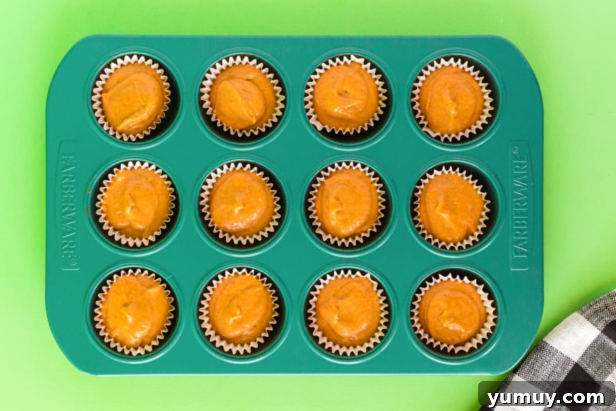 Rows of raw pumpkin cupcake batter neatly portioned into paper liners within a metal cupcake pan, awaiting their journey into the oven to transform into delicious treats.