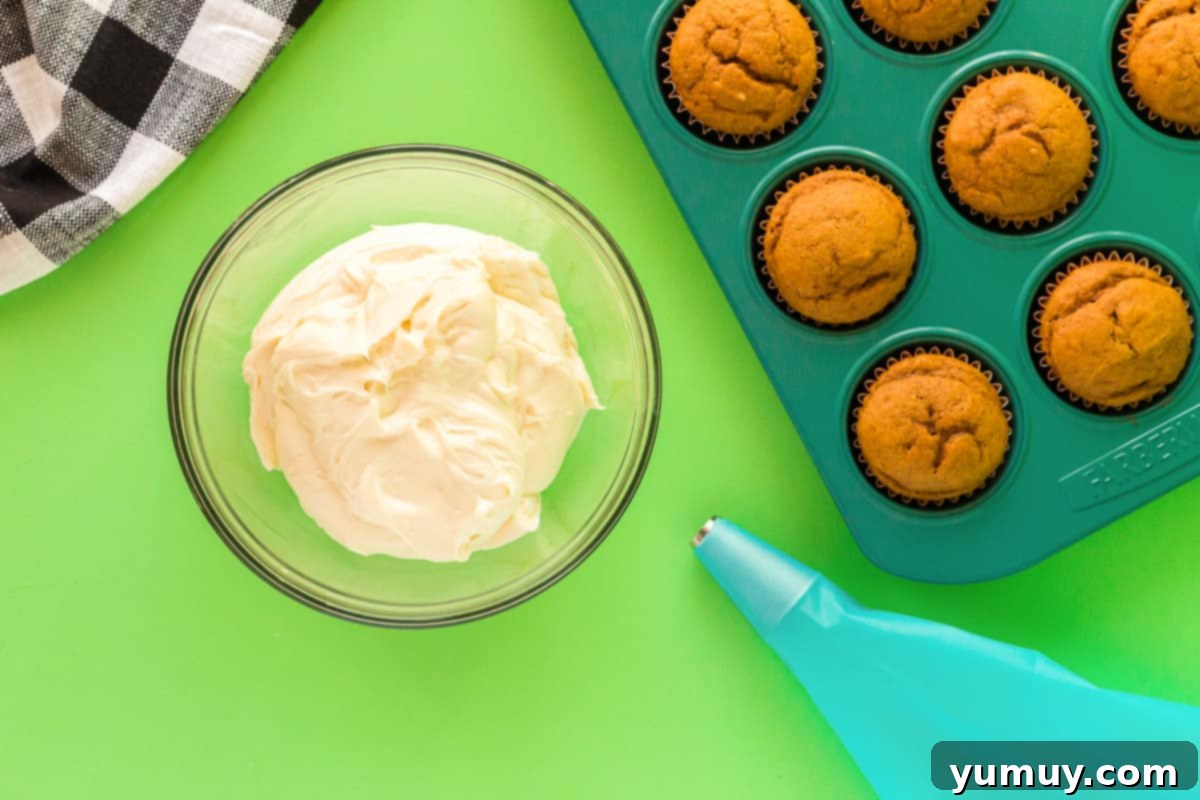 Smooth, white cream cheese frosting fills a clear mixing bowl, with a piping bag visibly ready to be filled, promising delicious decoration for baked goods.