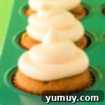 pumpkin cupcakes in a cupcake pan topped with cream cheese frosting