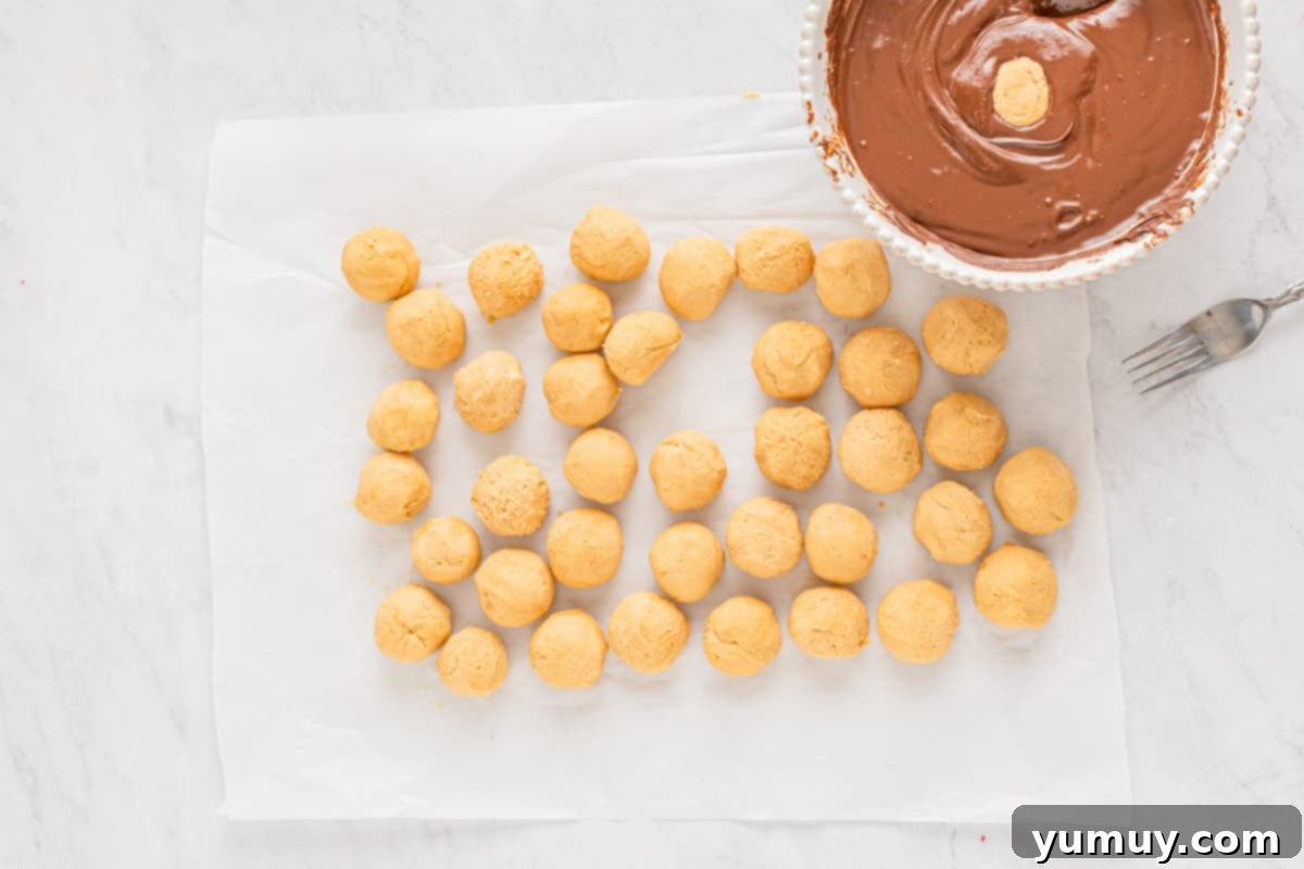Perfectly rolled buckeye candies sitting on parchment paper, next to a bowl of rich chocolate coating, ready for dipping.