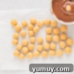Rolled peanut butter candies awaiting their chocolate dip, next to a bowl of melted chocolate coating.