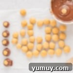 A rolled buckeye candy being dipped into a white bowl of chocolate coating using a toothpick.