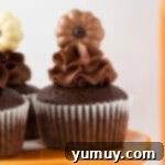 Close-up of three beautifully frosted chocolate pumpkin cupcakes on an orange cake stand, adorned with small chocolate pumpkins.
