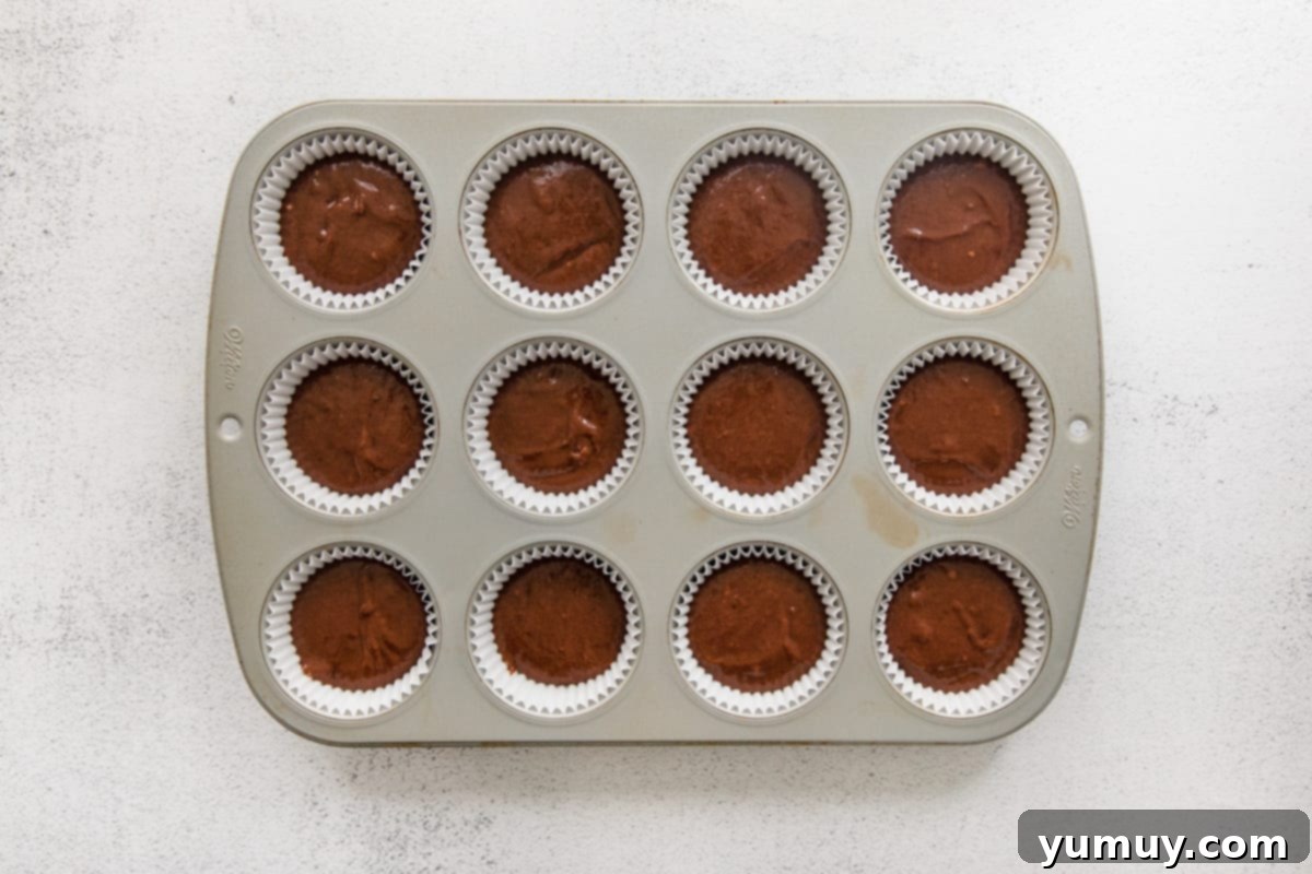 Muffin tin with paper liners, each precisely filled with the rich chocolate pumpkin cupcake batter, meticulously prepared and ready for the oven.