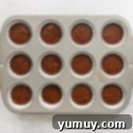 Muffin tin lined with paper liners and filled with chocolate pumpkin cupcake batter.