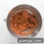 Overhead view of chocolate pumpkin cupcake frosting in a stainless mixing bowl, whipped to a light and fluffy consistency.