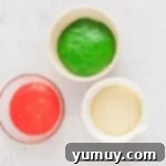 Three dough balls in bowls: one uncolored, one red, and one green, ready for rising